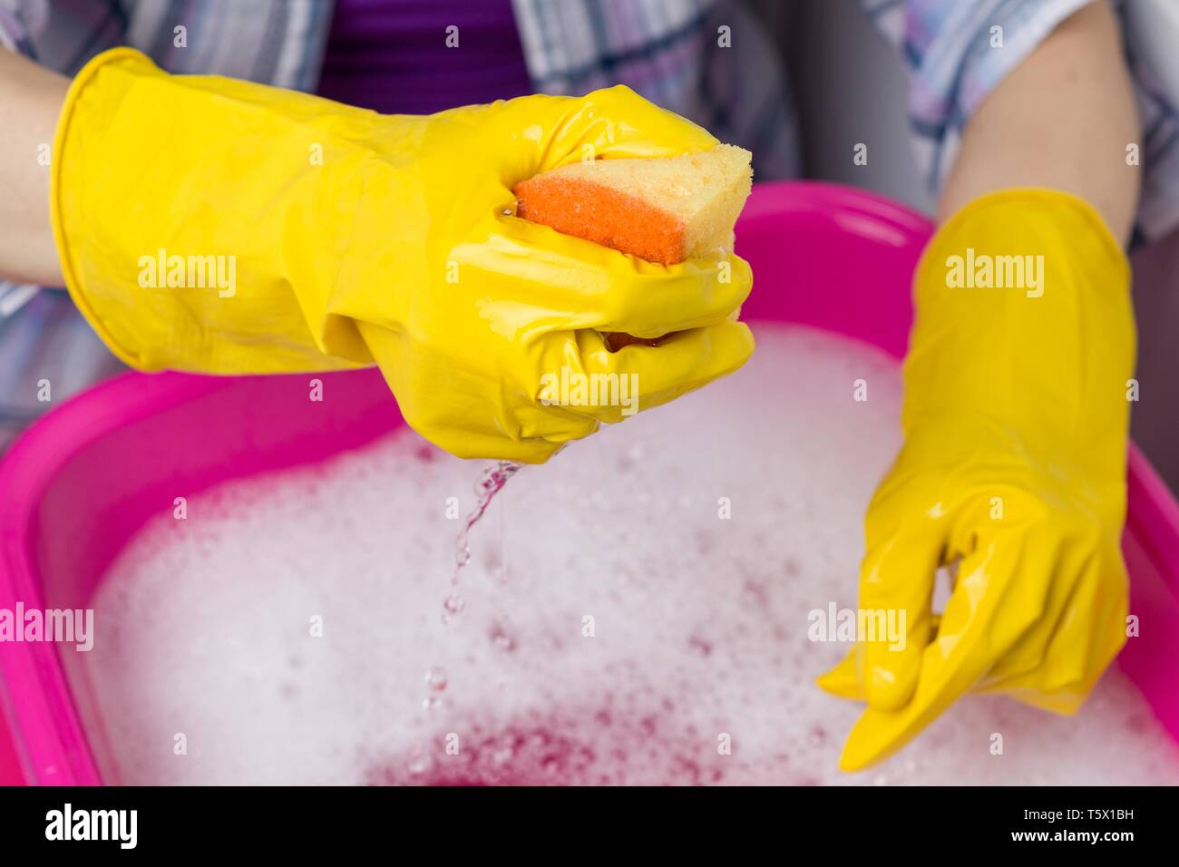 Nettoyage de la maison. Close-up du bassin avec de l'eau savonneuse, les mains dans les gants de protection en caoutchouc avec éponge Banque D'Images