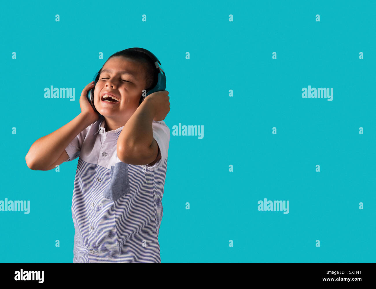 Jeune garçon dansant joyeusement à écouter de la musique sur le casque avec un fond bleu et copier l'emplacement pour un texte Banque D'Images
