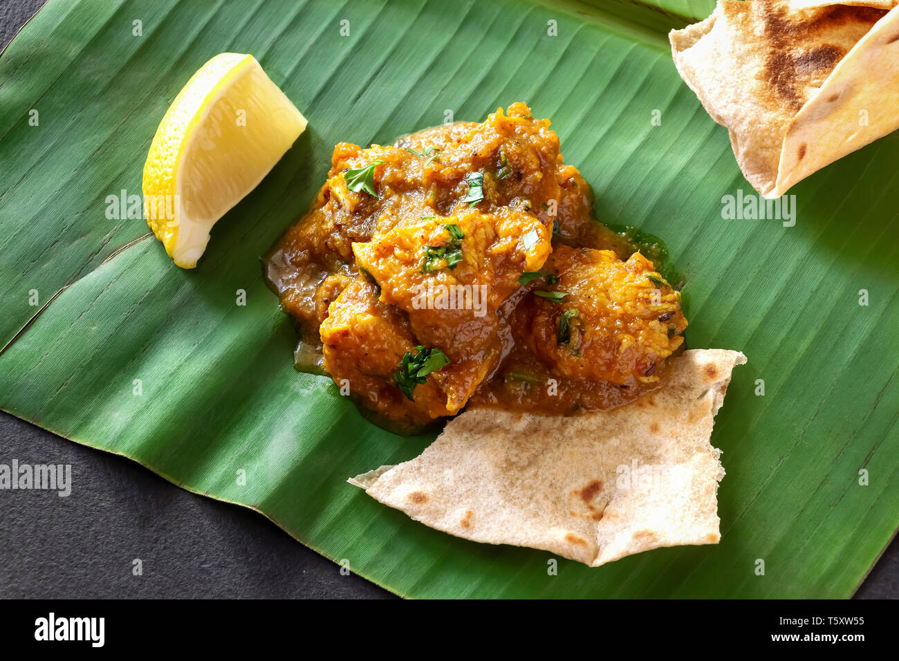 Close up beurre traditionnelle indienne poulet au curry et citron servi avec pain chapati sur feuille de bananier Banque D'Images