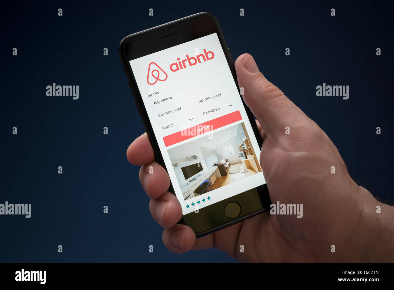 Un homme se penche sur son iPhone qui affiche le logo Airbnb (usage éditorial uniquement). Banque D'Images