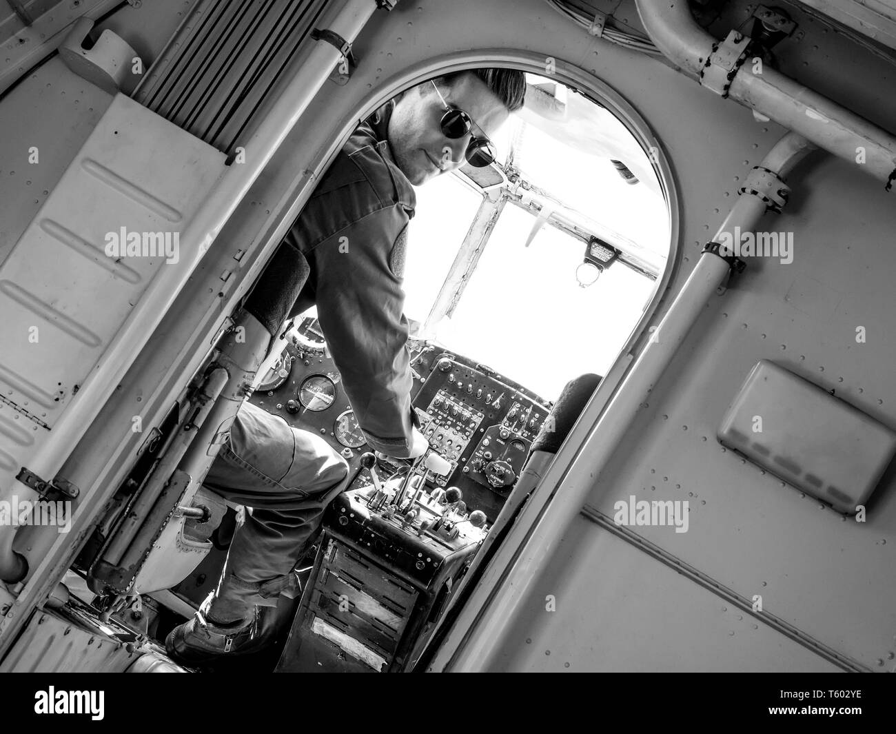 Un beau jeune homme dans un ensemble vert pilote assis dans le cockpit d'un vieil avion sur une journée ensoleillée. Banque D'Images