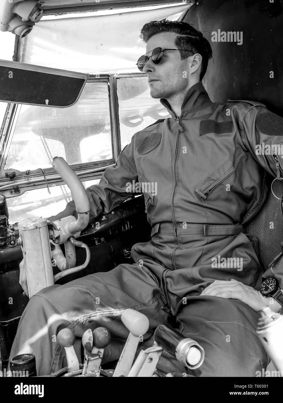 Un beau jeune homme dans un ensemble vert pilote assis dans le cockpit d'un vieil avion sur une journée ensoleillée. Banque D'Images