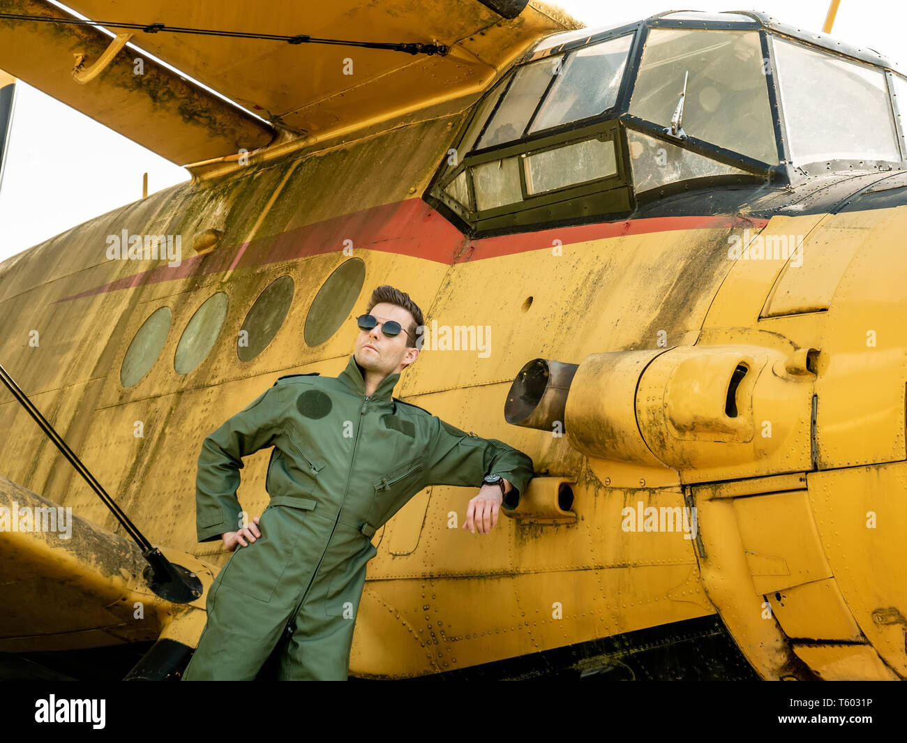 Un beau jeune homme pilote dans un ensemble vert debout à côté d'un vieil avion sur une journée ensoleillée. Banque D'Images