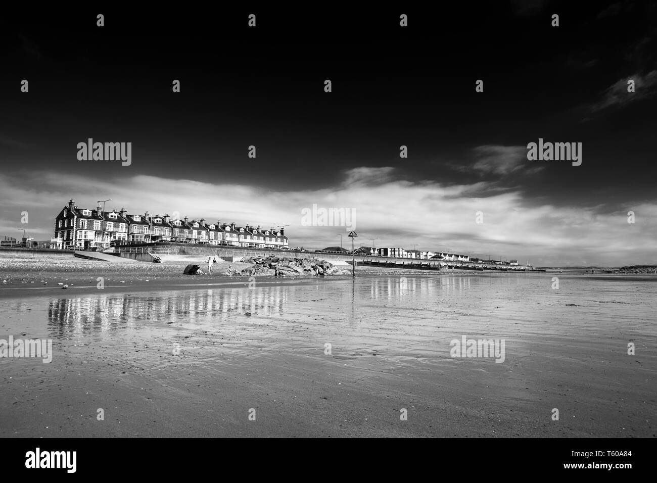 Les bâtiments côtiers et réfléchi sur la promenade victorienne sur le sable humide. Tywyn au milieu du Pays de Galles, Royaume-Uni. Edit monochrome Banque D'Images