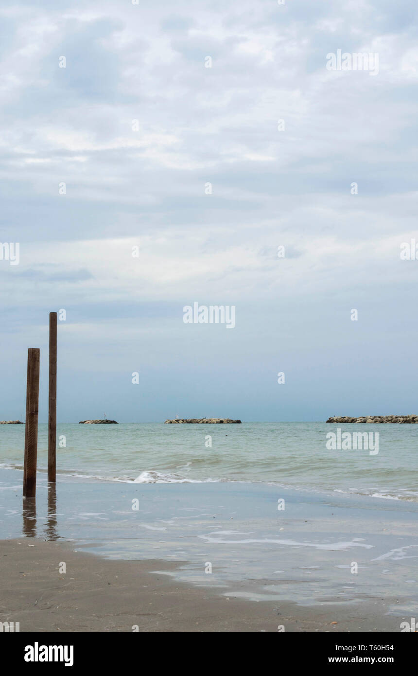 Poteaux en bois et des pierres sur une plage sous un ciel nuageux sy Banque D'Images