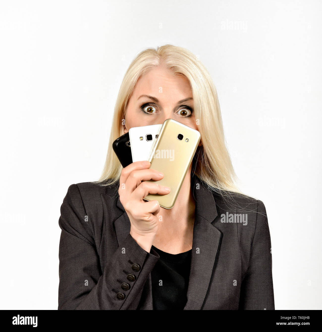 Femme d'affaires à la recherche sur le dessus de trois téléphones mobiles avec de grands yeux Banque D'Images