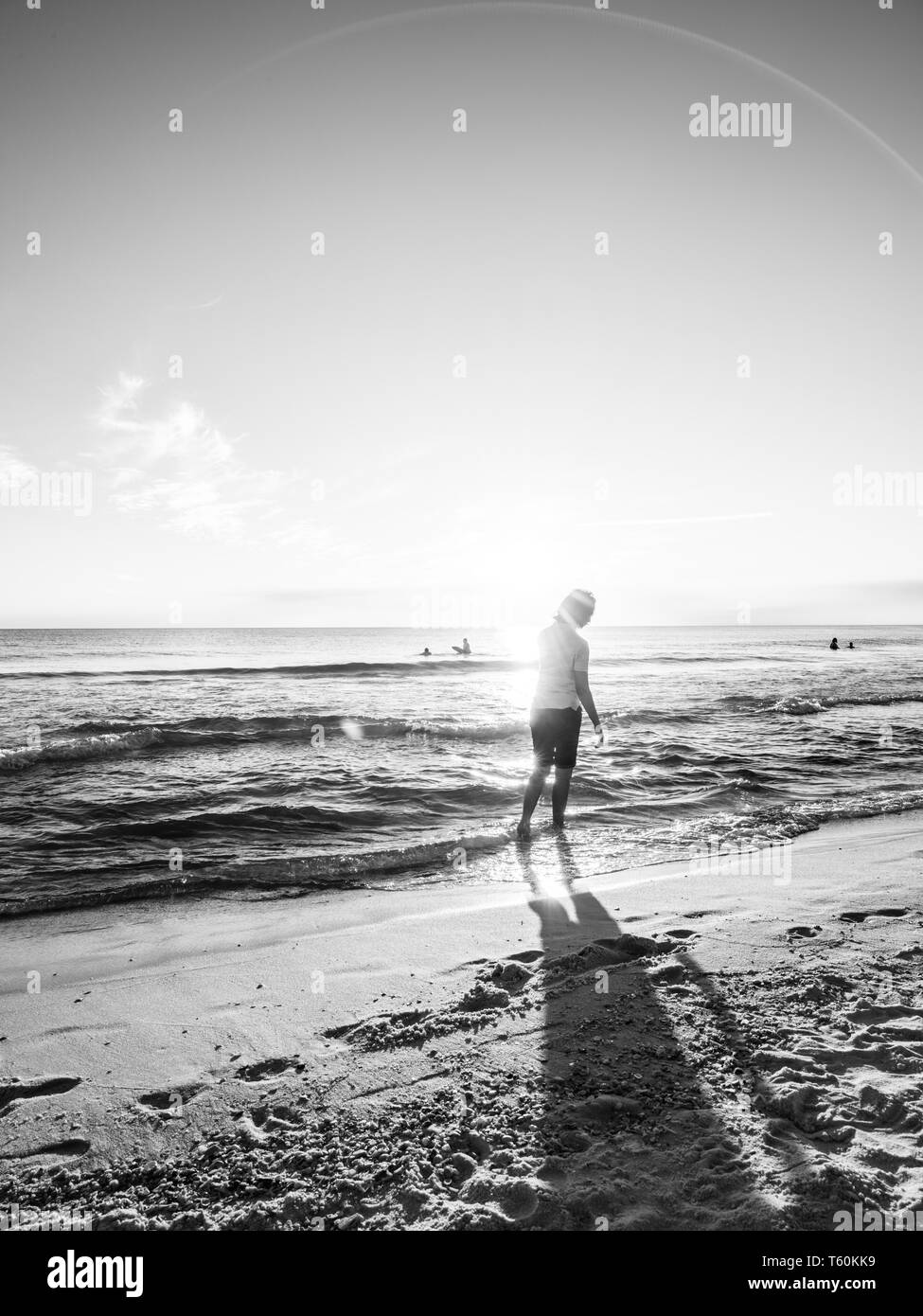 Une seule personne marchant dans le surf au coucher du soleil. Banque D'Images