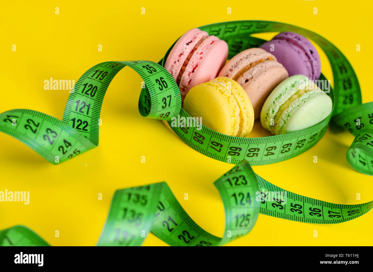 Mètre à ruban vert et macarons ou macarons sur fond jaune. La perte de poids et le traitement minceur concept. Vue d'en haut Banque D'Images