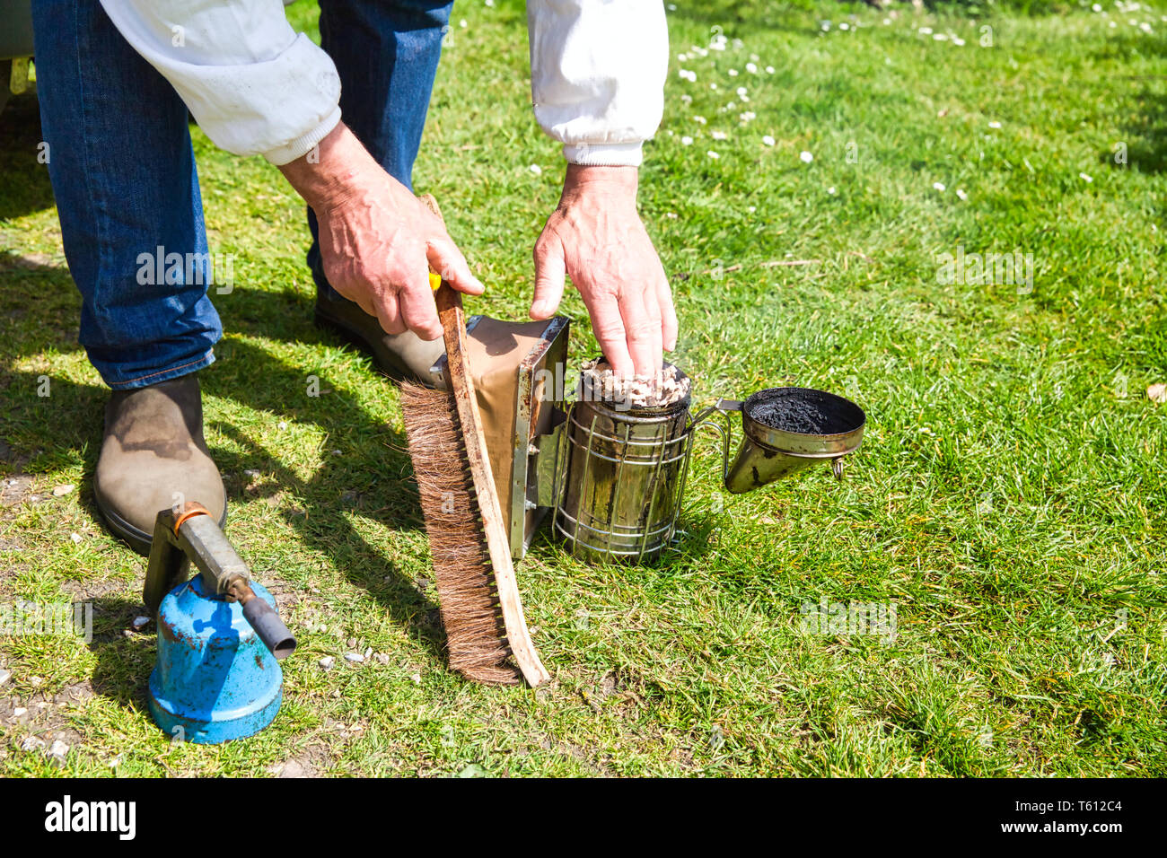 Part de l'apiculteur de vêtements de protection mise en marche de l'ancien fumeur à l'aide d'un pinceau sur l'herbe jardin. Fumée secondaire pour transférer les abeilles, de visiter une ruche. Tr authentique Banque D'Images