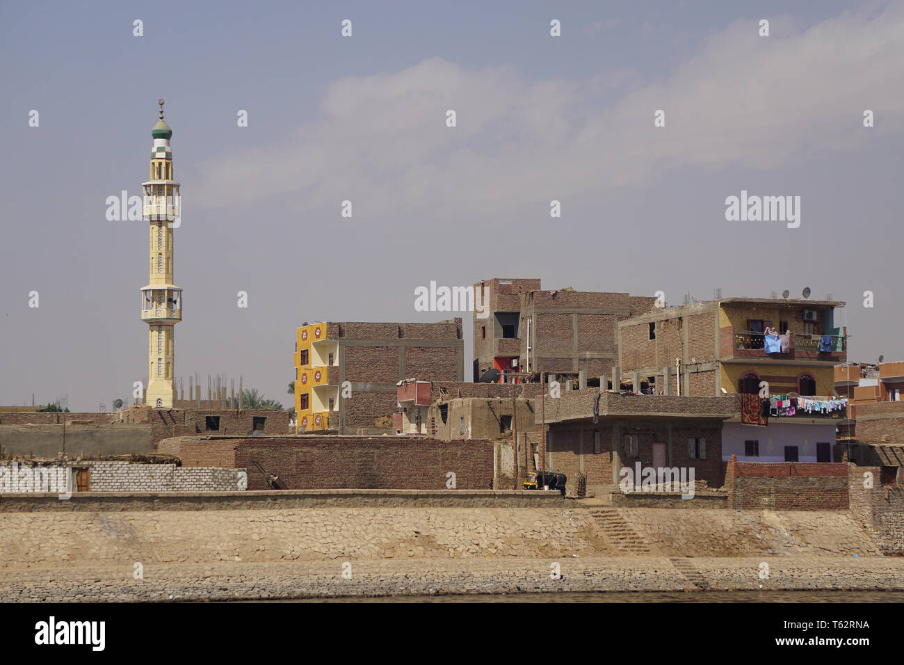 Nil, Égypte : maisons colorées, tapis et vêtements séchant au soleil, et un minaret le long de la rive est du Nil. Banque D'Images