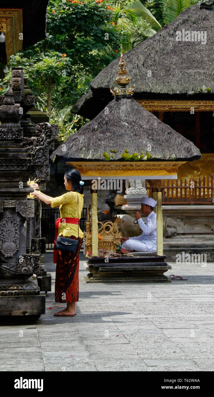 Chef de prière dans une petite cabine derrière une femme éteindre les offres de fleurs en premier plan, Pura temple Tirta Empul, Ubud, Indonésie Banque D'Images