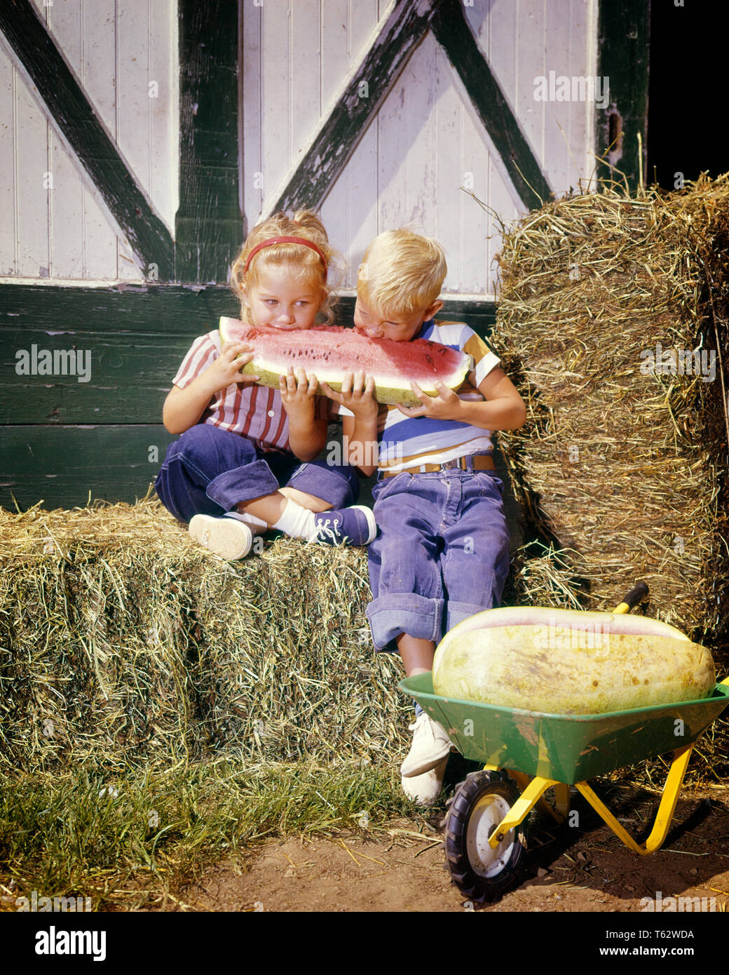 1960 garçon fille blonde FRÈRE ET SŒUR SITTING ON BALE OF HAY PARTAGE DE LA GRANDE TRANCHE DE MELON D'EAU À L'EXTÉRIEUR GRANGE ESTIVALES - kf3084 HAR001 vie d'équipe de HARS GRANGE FRÈRES Femelles Mâles COPIE ESPACE RURAL AGRICULTURE FRÈRES SOEURS TRANCHE D'ÉTÉ LE BONHEUR DE LA TÊTE ET DES ÉPAULES ET DE PASTÈQUE SUR SŒUR ÉLÉGANT CONCEPTUEL BLEU JEANS DE BALLE juvéniles de la coopération l'origine ethnique caucasienne SOLUTIONS HAR001 old fashioned Banque D'Images