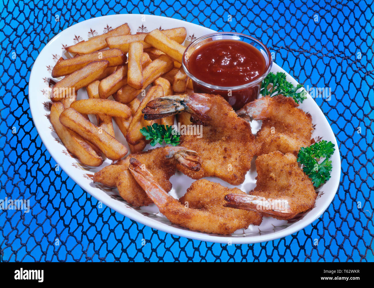 1970 PAPILLON PANÉS CREVETTES FRITS SAUCE COCKTAIL SUR LE PLATEAU ET DE FRITES FOND BLEU COUVERT DE FILET DE PÊCHE - kf4889 TRAF001 COQUILLAGES HARS Banque D'Images