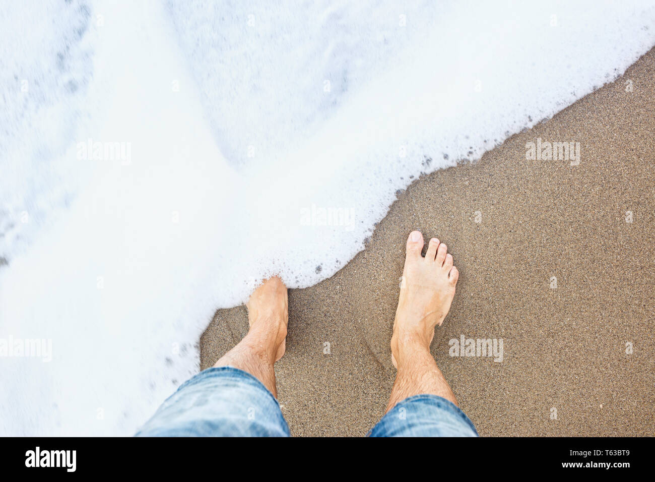 Les pieds de l'homme sur le sable sur le littoral. Banque D'Images