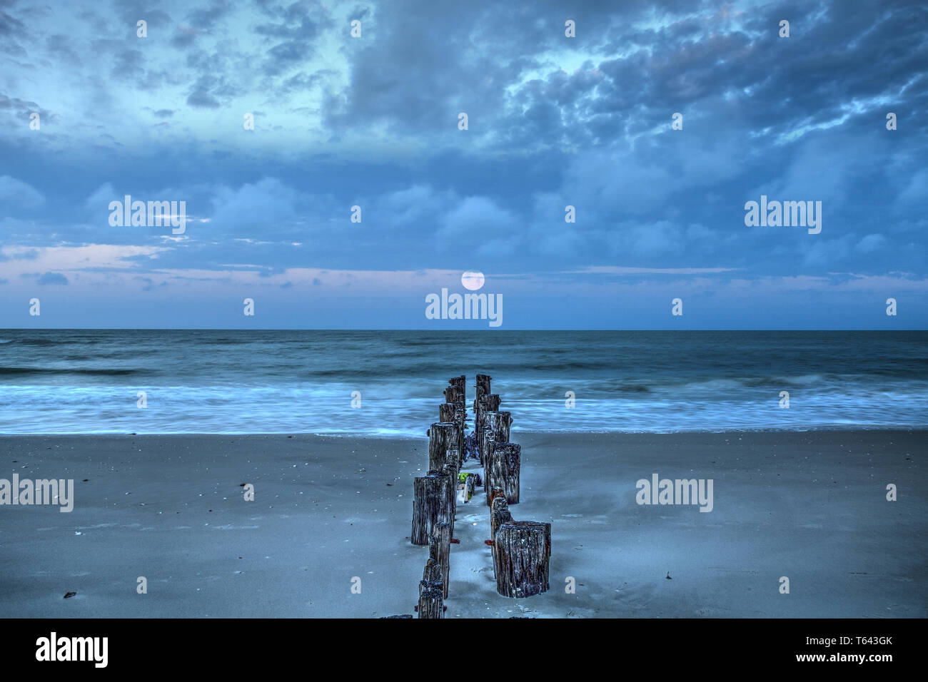 La lune à l'aube sur une jetée en ruine sur la plage de Port Royal de Naples, en Floride. Banque D'Images