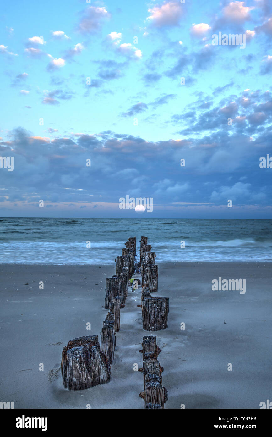 La lune à l'aube sur une jetée en ruine sur la plage de Port Royal de Naples, en Floride. Banque D'Images