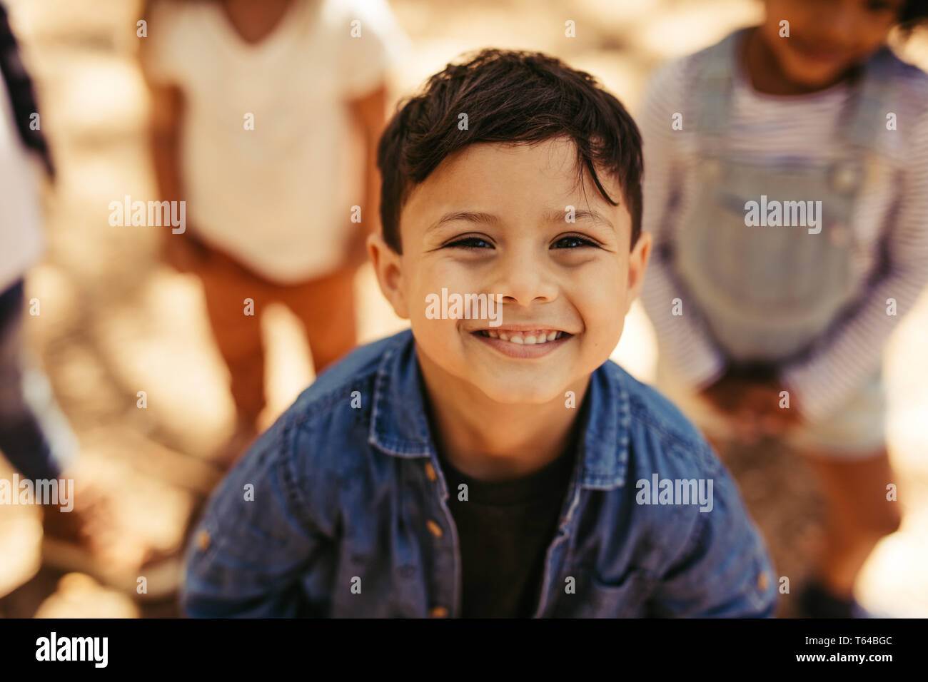 Close up portrait of cute boy smiling at camera avec des amis à l'arrière-plan. Kid avec des amis à l'extérieur. Banque D'Images
