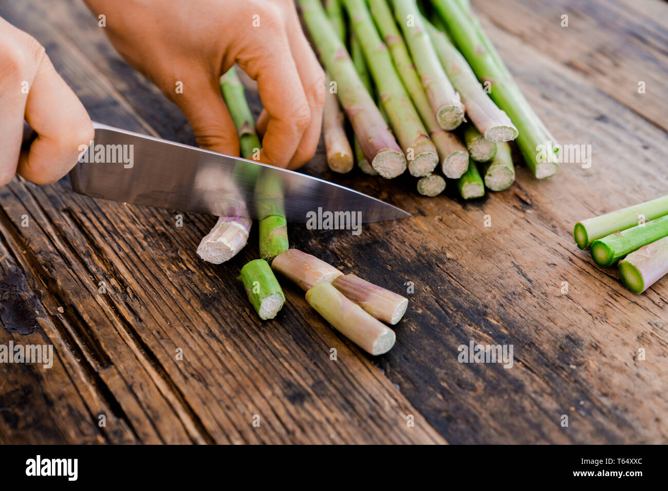 Coupe femme cuisinière et la préparation de l'asperge verte avec un couteau bien aiguisé sur une surface en bois rustique Banque D'Images