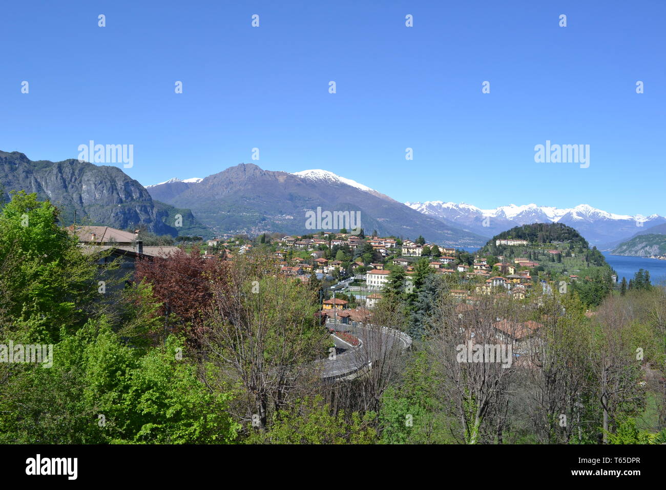Belle vue sur la péninsule de Bellagio à ressort avec une ville, Alpes européennes avec de la neige sur les sommets et le lac de Côme à partir de la route de Lecco dans une journée ensoleillée. Banque D'Images