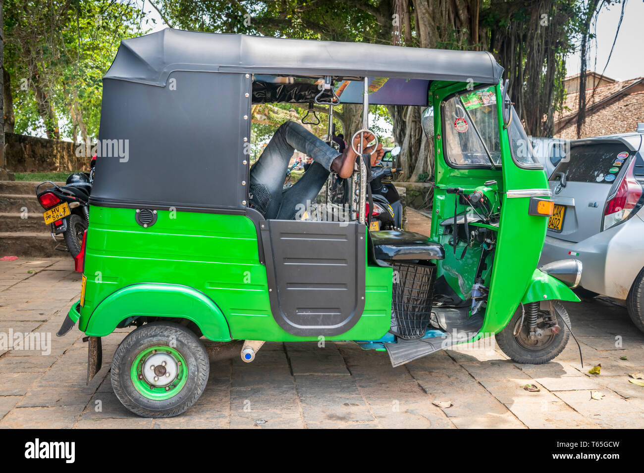 Le conducteur d'un vert lumineux Tuk Tuk met ses pieds et prend une pause dans la ville de Galle au Sri Lanka. Banque D'Images