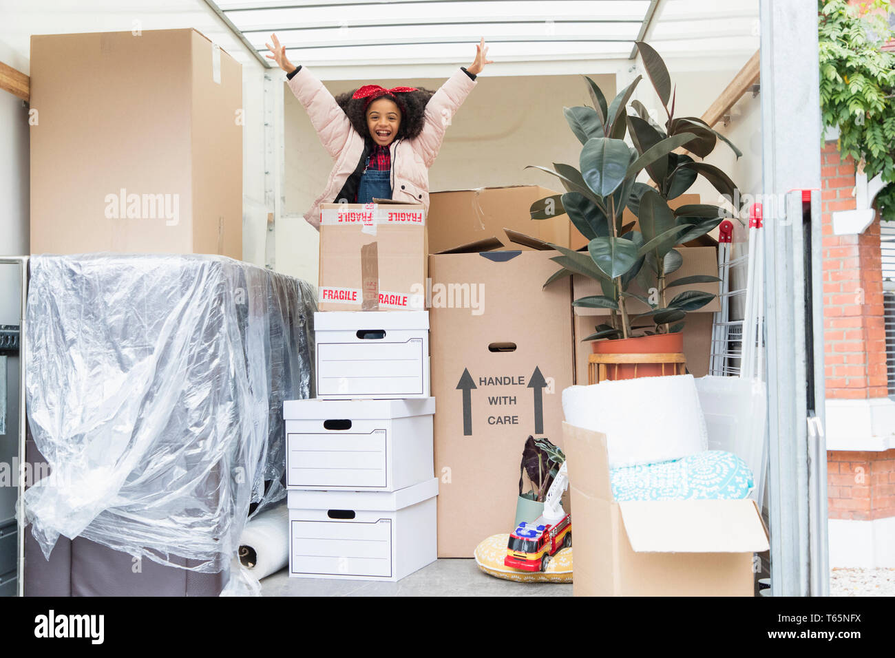 Portrait playful girl jumping venant de l'arrière des boîtes de carton en camion de déménagement Banque D'Images