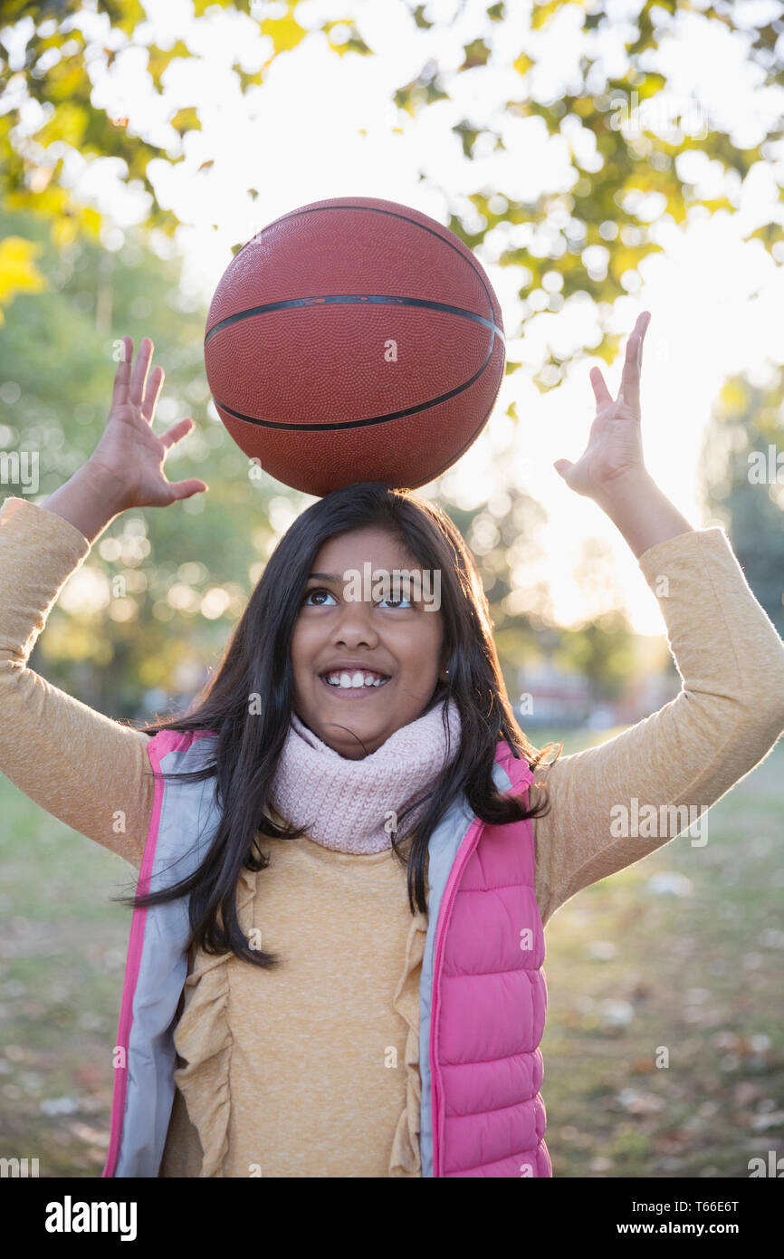 Portrait cute girl balancing basket-ball sur la tête in autumn park Banque D'Images