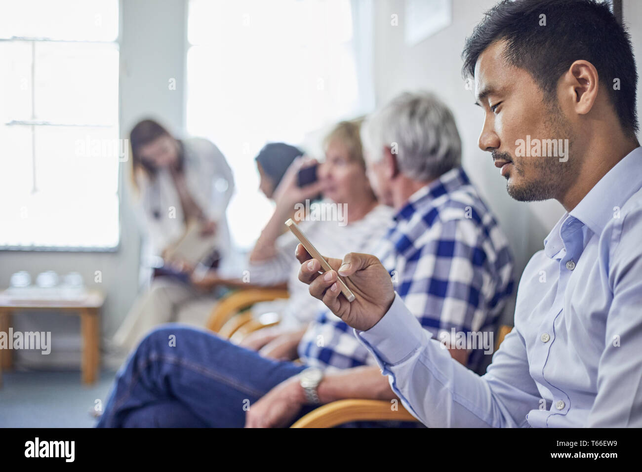 L'homme à l'aide de smart phone, l'attente dans la salle d'attente de la clinique Banque D'Images