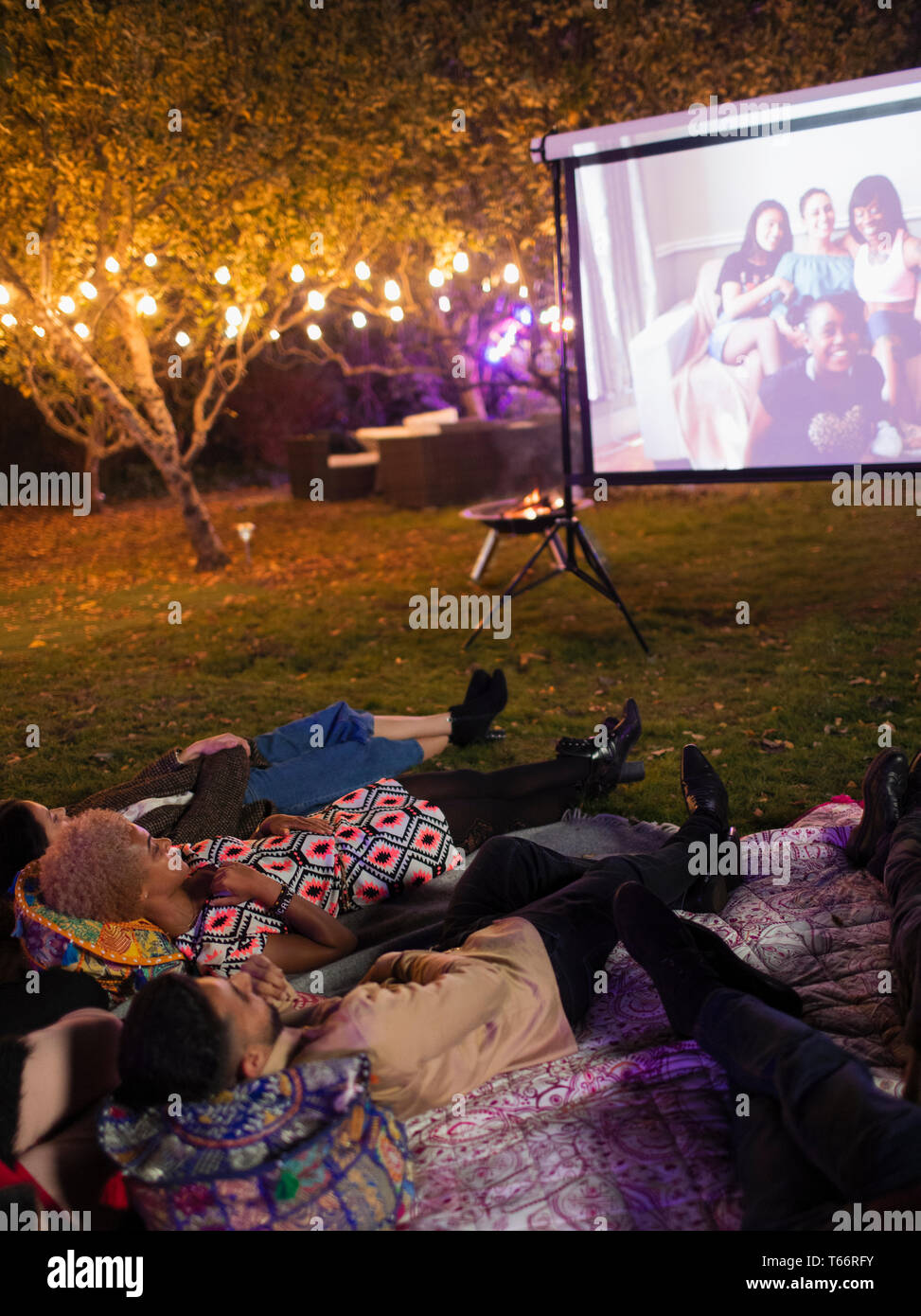 Les amis se détendre, regarder la vidéo sur l'écran de projection in backyard Banque D'Images