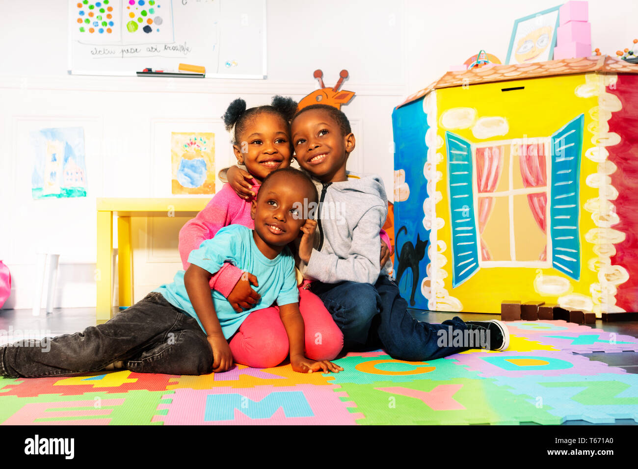 Groupe de trois garçons et une fille heureuse en maternelle hugging ensemble Banque D'Images