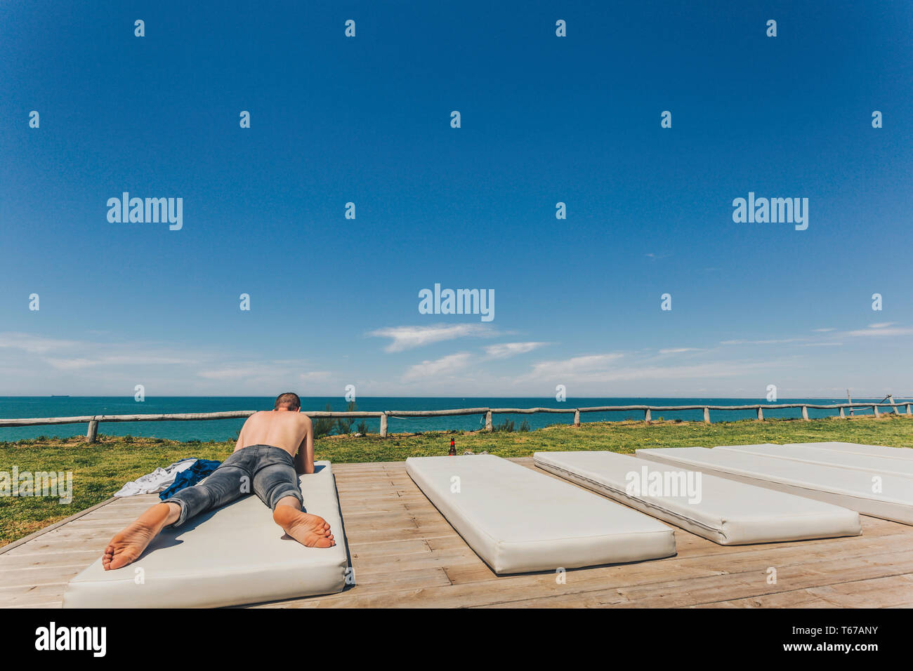 Portrait jeune homme torse nu et en jeans couché sur la plage sur un matelas blanc avec la mer et le ciel en arrière-plan, copy space Banque D'Images