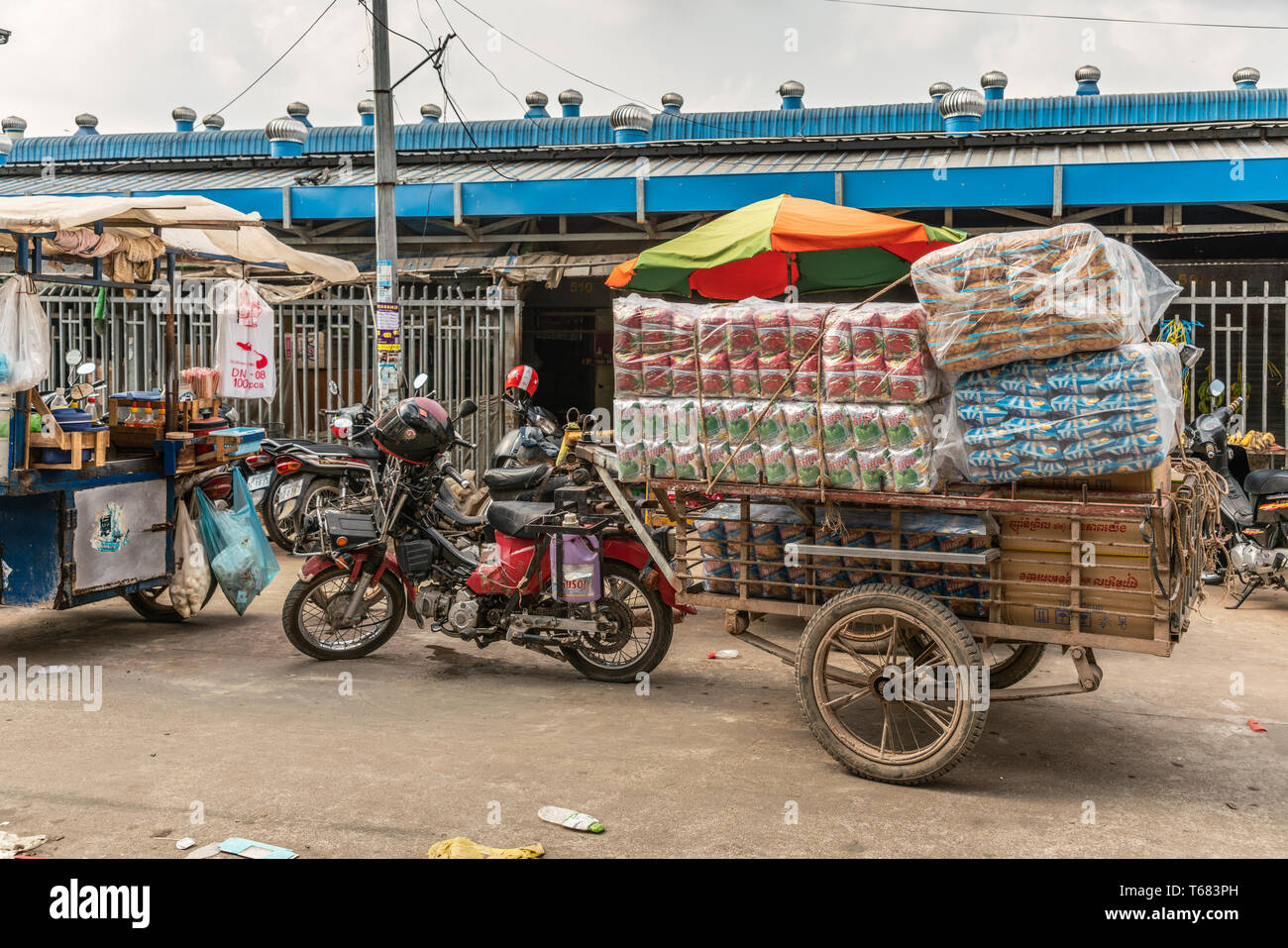 Sihanoukville, Cambodge - Mars 15, 2019 : Marché Phsar Leu. Remorque en bois brun rouge connecté à moto considérablement chargé de gros paquets de nourriture Banque D'Images