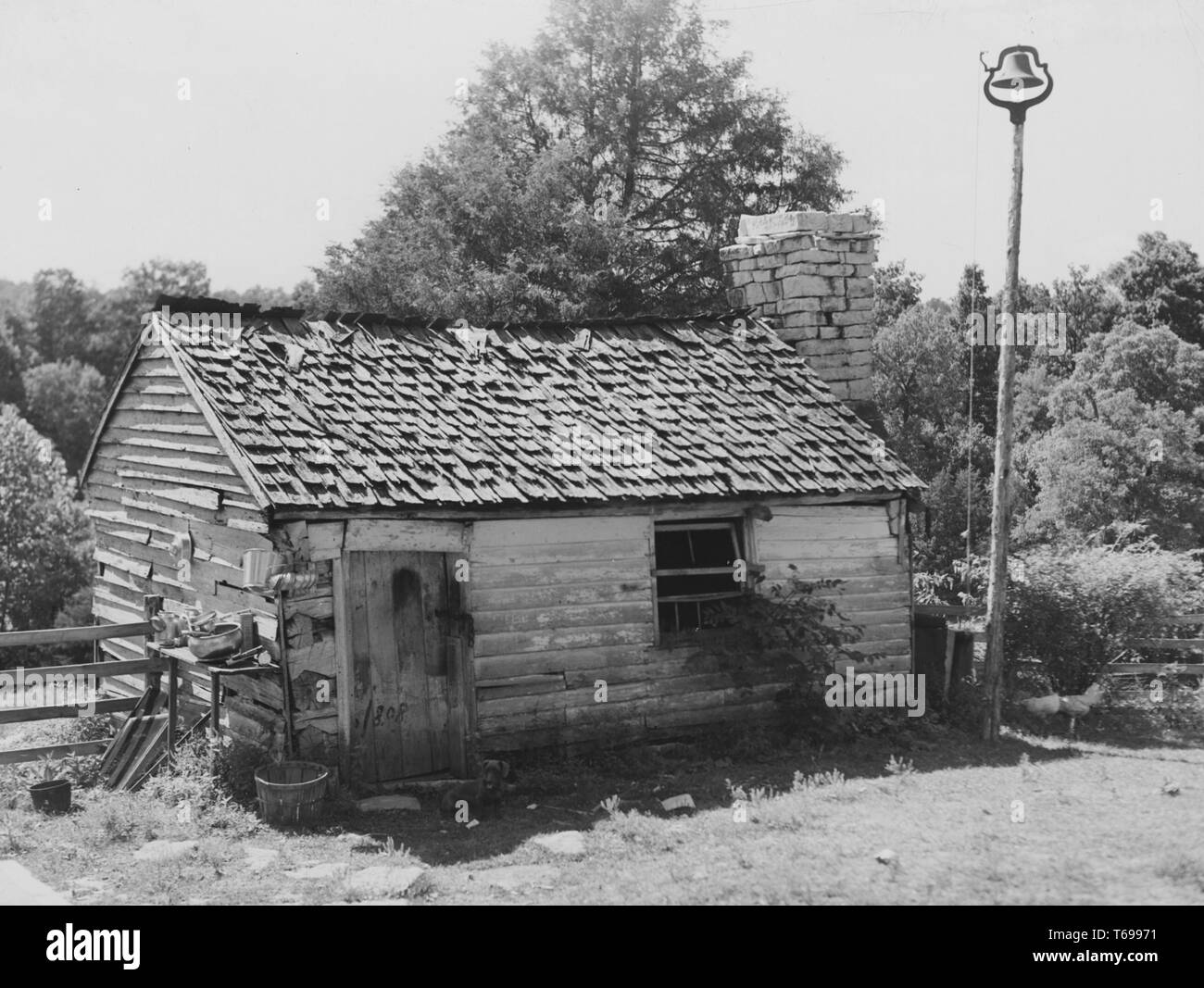 Photographie en noir et blanc d'une petite cabane en bois, avec un toit de bardeaux, cheminée en brique, et d'une bell situé au sommet d'un grand poteau à droite, probablement un ancien esclave quarts qui a été converti pour être utilisé comme une installation de stockage de produits laitiers lait connu comme une chambre ou un dépôt ; situé dans Bardstown, Kentucky, USA ; photographié par Marion Post Wolcott, sous le parrainage des États-Unis' Farm Security Administration, août 1940. À partir de la Bibliothèque publique de New York. () Banque D'Images