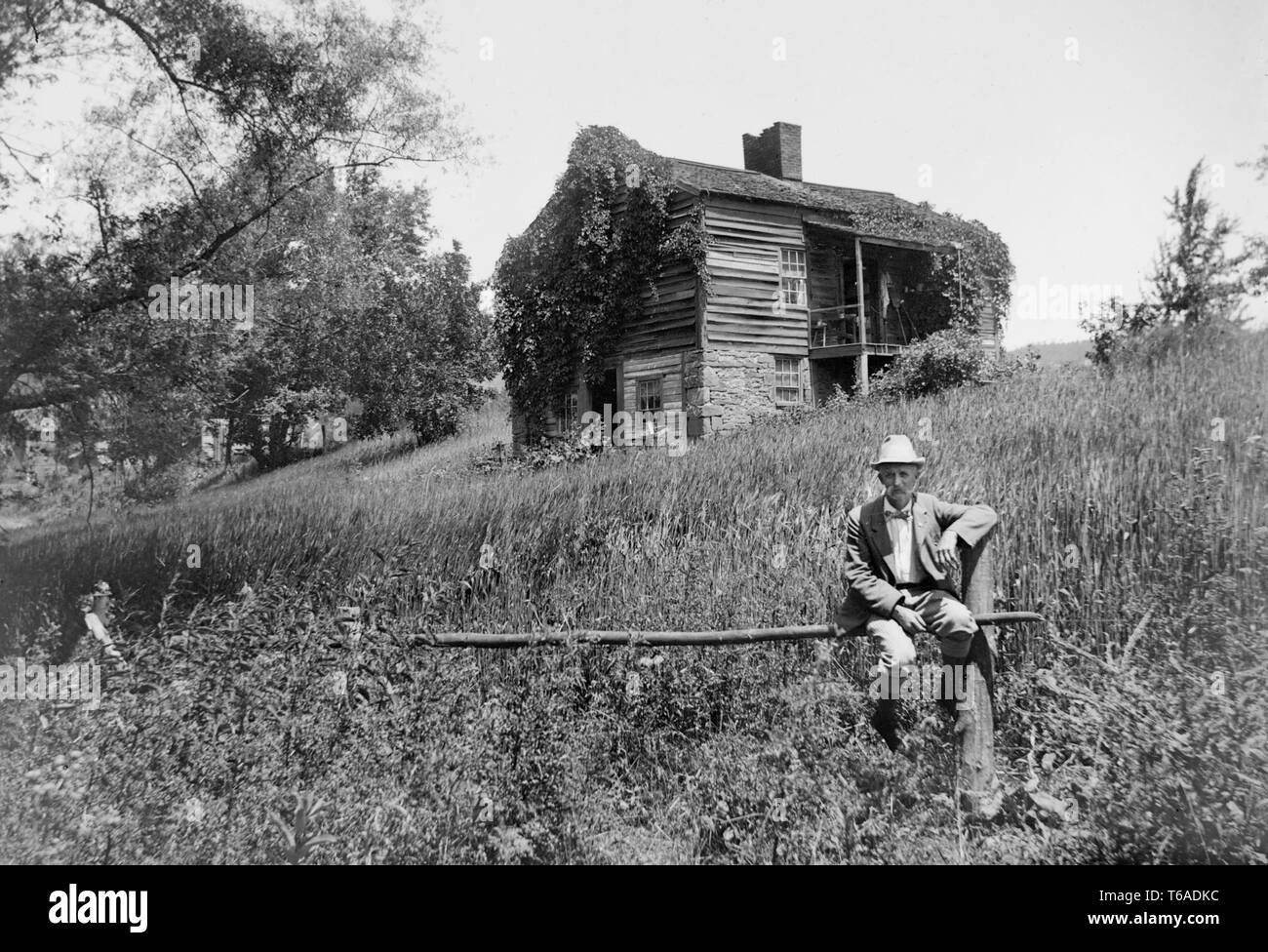 Un homme est assis sur une clôture à l'extérieur de sa maison en Pennsylvanie, ca. 1910. Banque D'Images