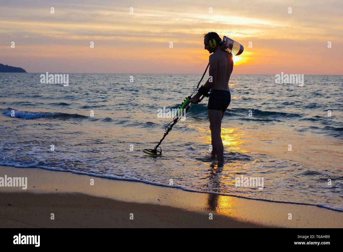 Chasseur de trésor avec détecteur de métal sur la plage au coucher du soleil Banque D'Images