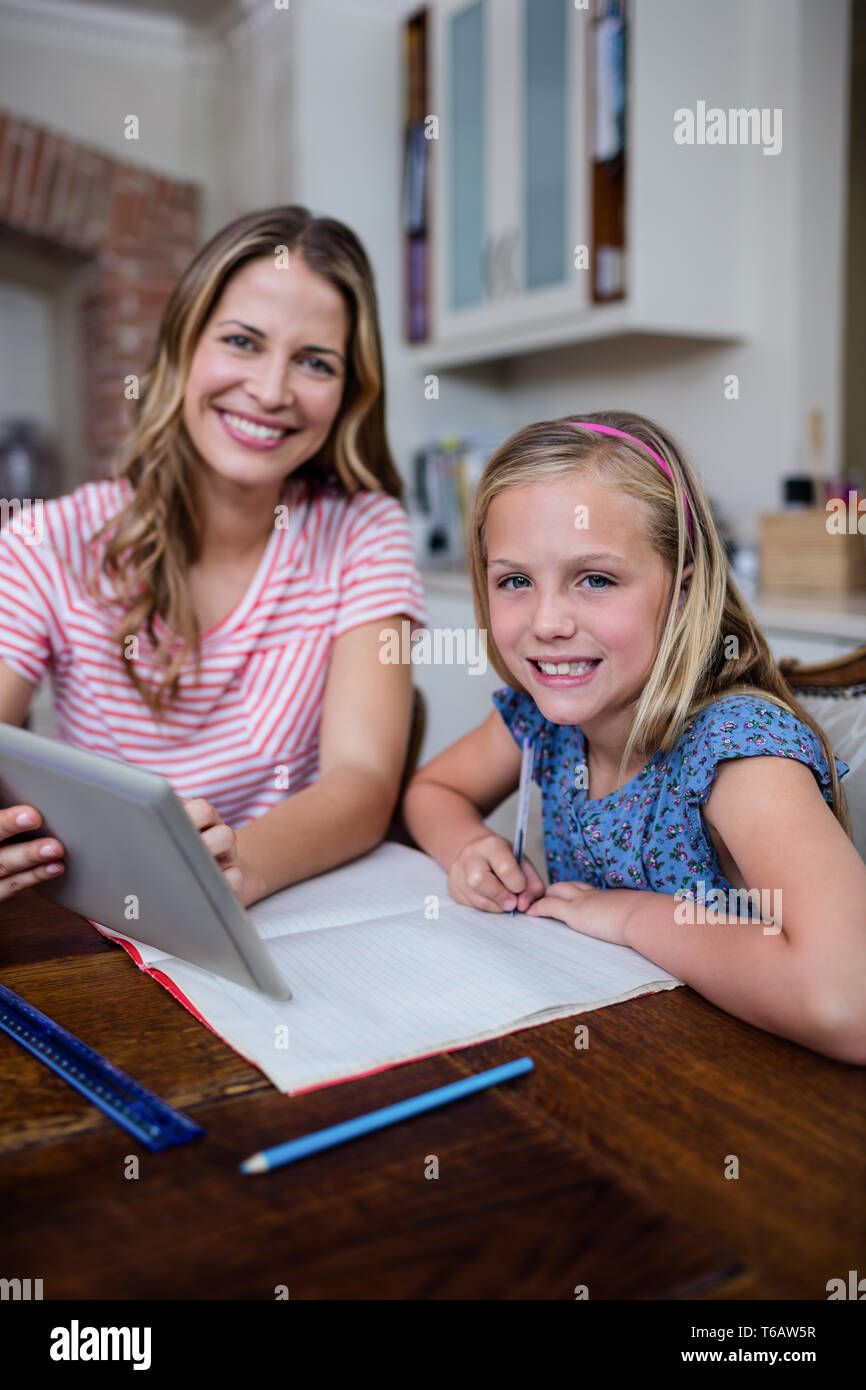 Mère à l'aide d'une tablette numérique tout en aidant sa fille avec ses devoirs Banque D'Images