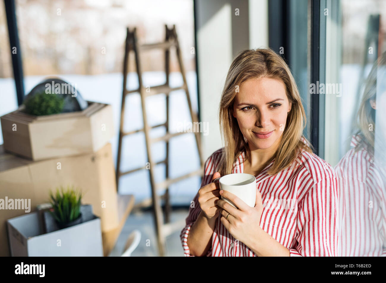 Un jeune femme déménagement à new home, appuyé sur une fenêtre et boire du café. Banque D'Images