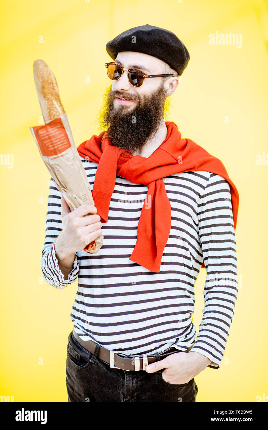 Portrait d'un homme habillé en élégant style français avec chemise rayée, chapeau et foulard rouge sur le fond jaune Banque D'Images