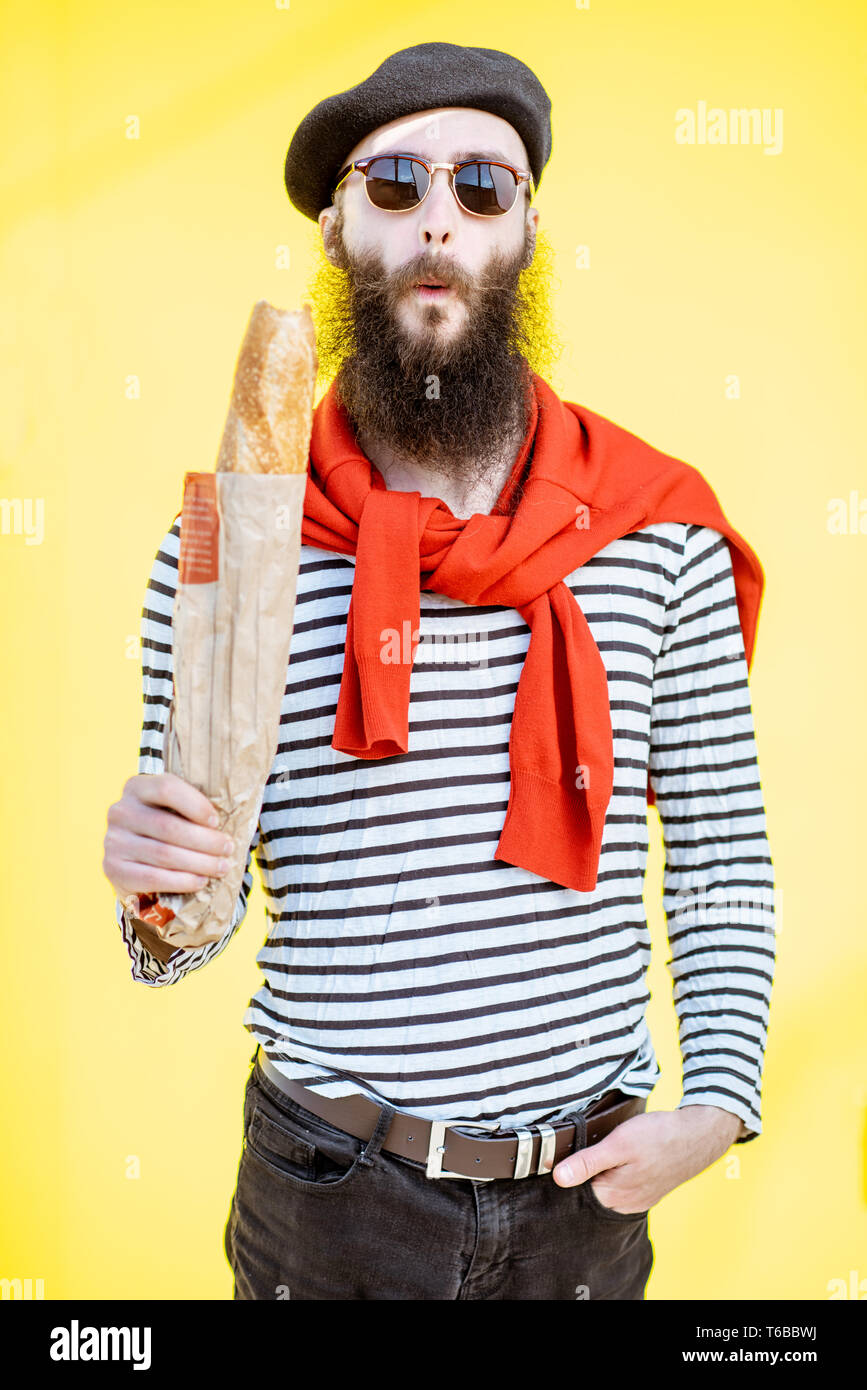 Portrait d'un homme habillé en élégant style français avec chemise rayée, chapeau et foulard rouge sur le fond jaune Banque D'Images