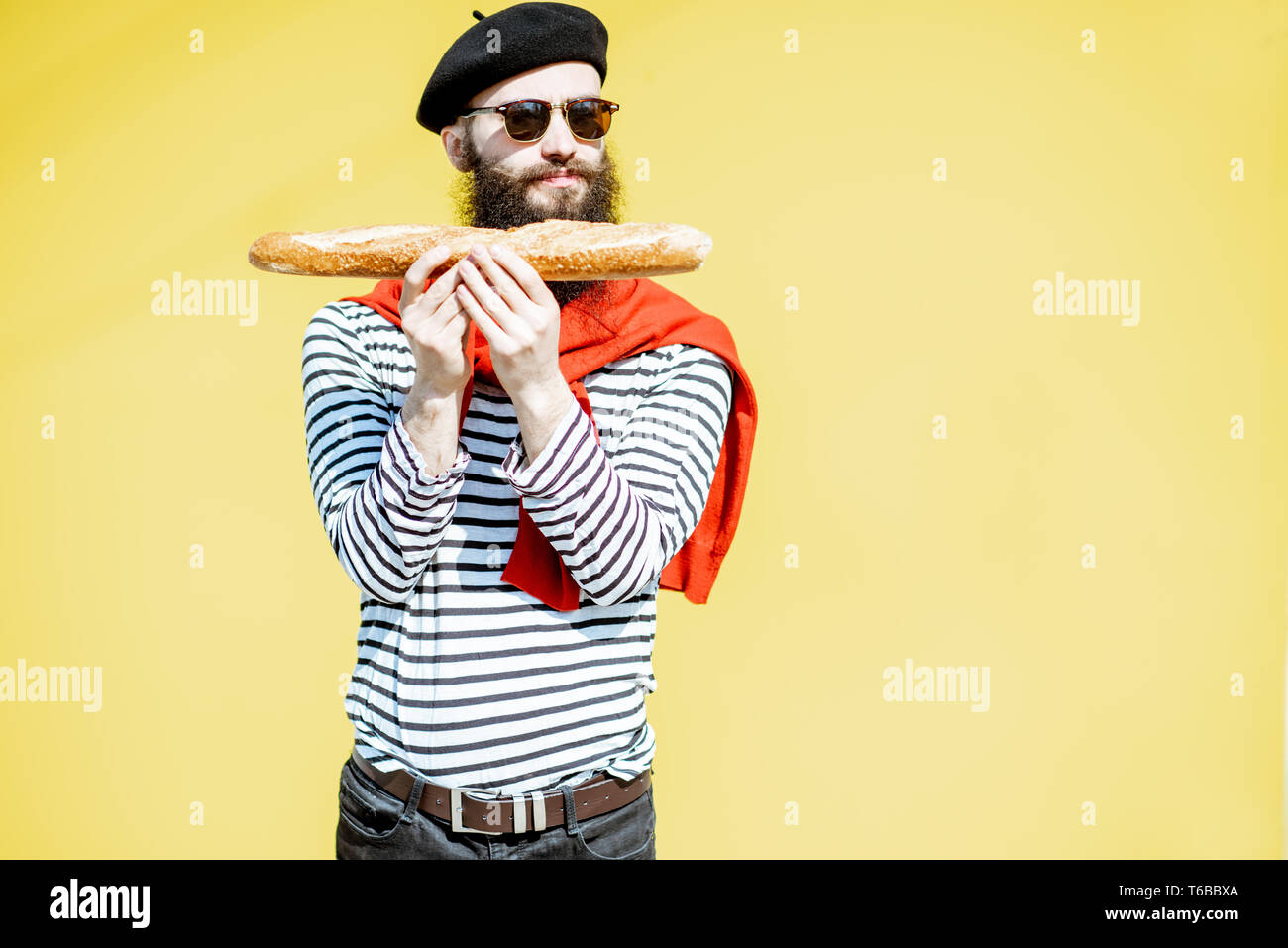 Portrait d'un homme habillé en élégant style français avec chemise rayée, chapeau et foulard rouge sur le fond jaune Banque D'Images