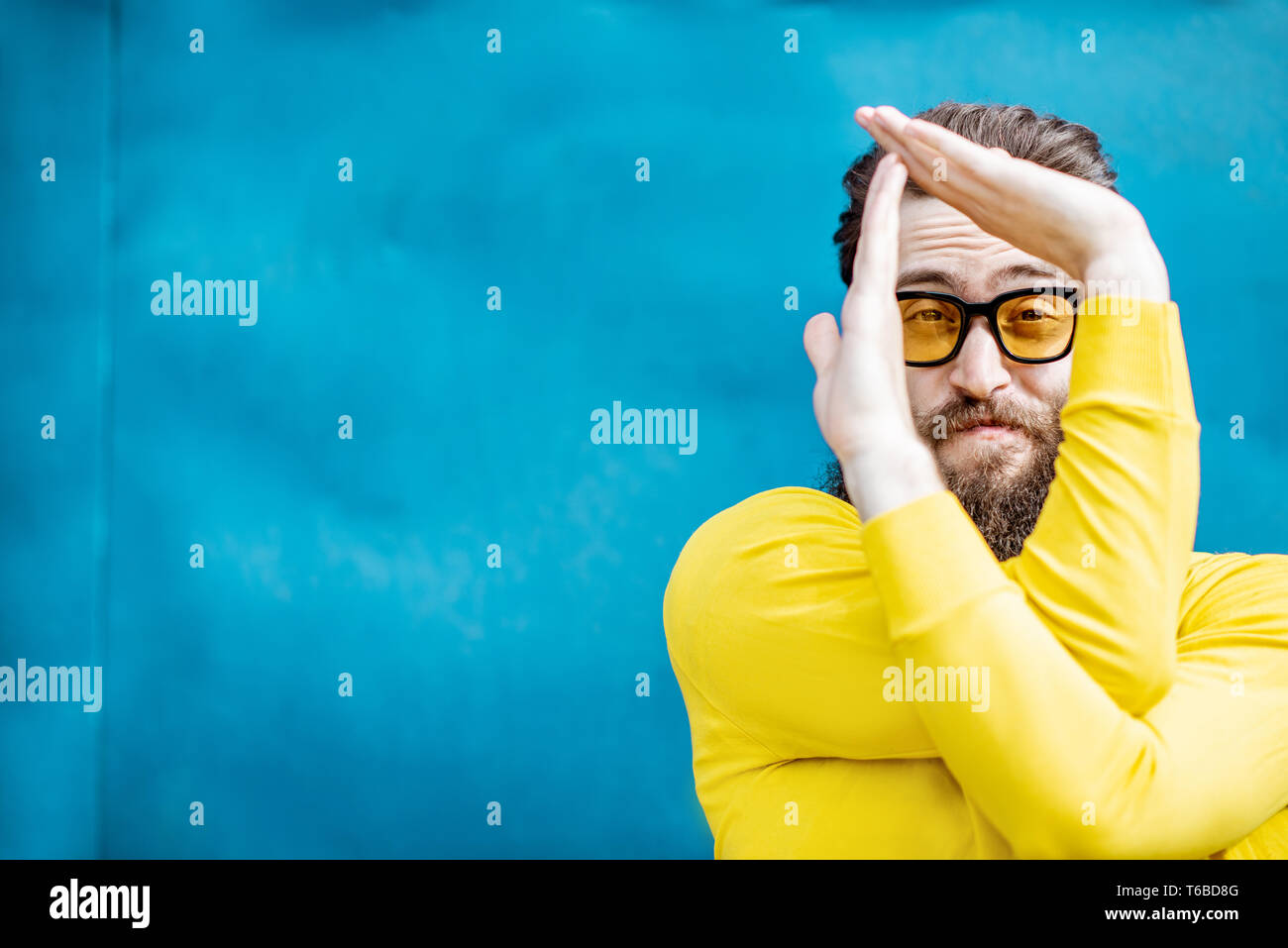 Portrait d'un homme barbu en élégant chandail jaune et des lunettes de soleil sur le fond bleu Banque D'Images