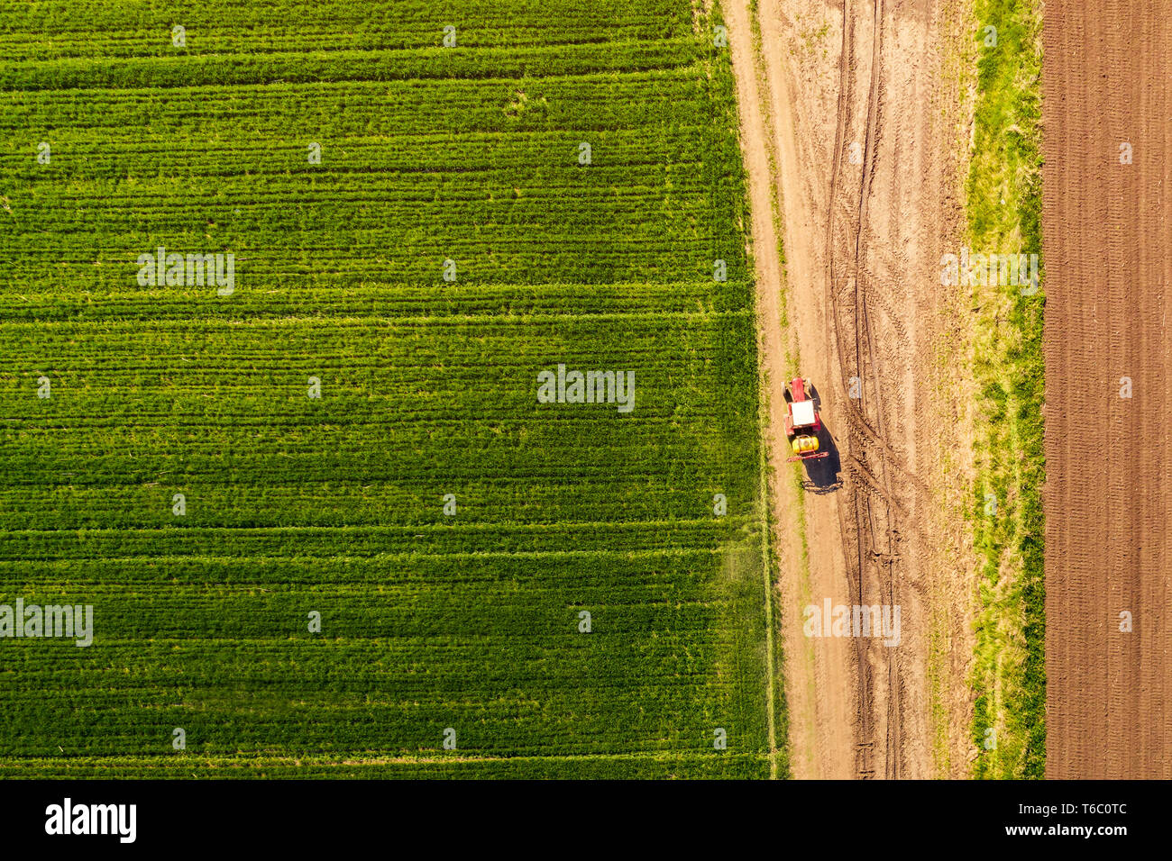 Vue aérienne de tracteur avec pulvérisateur ci-joint sur la route de campagne en direction du domaine, de haut en bas vue du pov de drones Banque D'Images