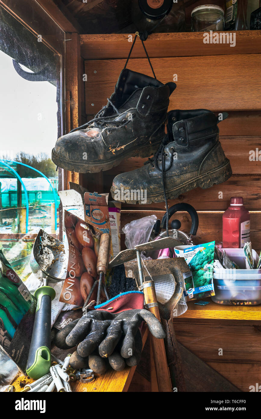 Intérieur d'un abri de jardin avec une paire de bottes noires, quelques outils de jardinage et les paquets de semences, à côté d'une fenêtre avec l'attribution à l'extérieur, jardins Banque D'Images