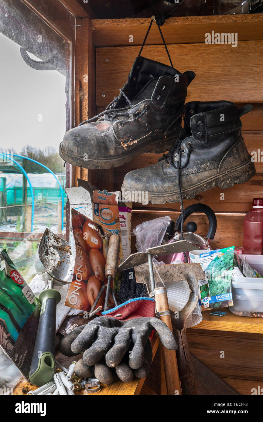 Intérieur d'un abri de jardin avec une paire de bottes noires, quelques outils de jardinage et les paquets de semences, à côté d'une fenêtre avec l'attribution à l'extérieur, jardins Banque D'Images