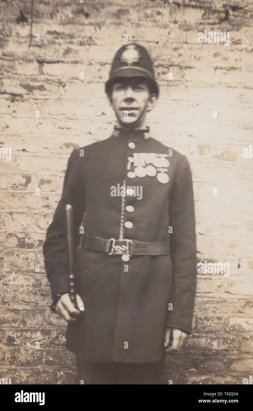 Vintage Photo d'un policier britannique se tenait devant un mur tenant sa matraque et arborant fièrement ses médailles. Banque D'Images