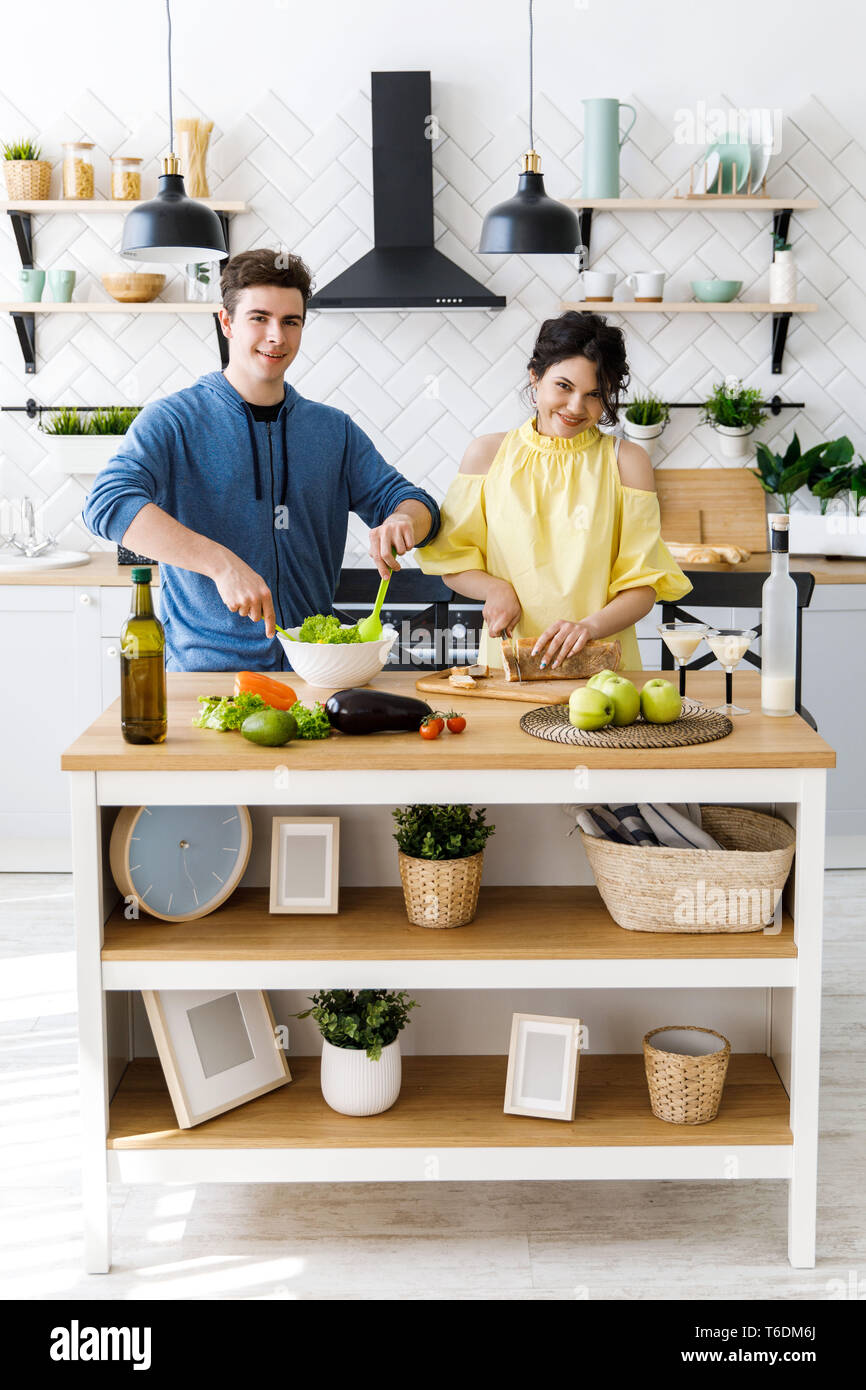 Beau couple dans la cuisine. Bel homme est en train de préparer une salade pendant que sa petite amie est la coupe du pain, les deux sont smiling Banque D'Images