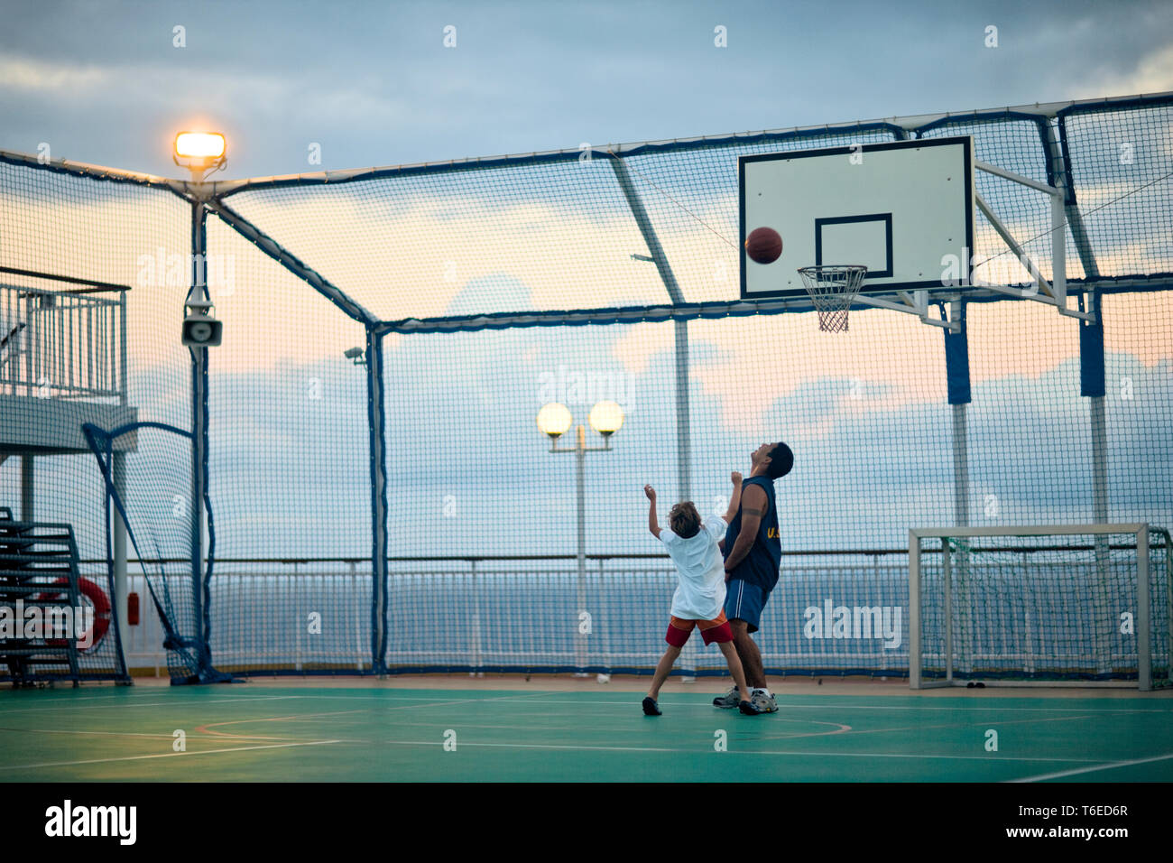 Montres homme comme un garçon jette une basket-ball au hoop sur une mer clôturé de basket-ball. Banque D'Images