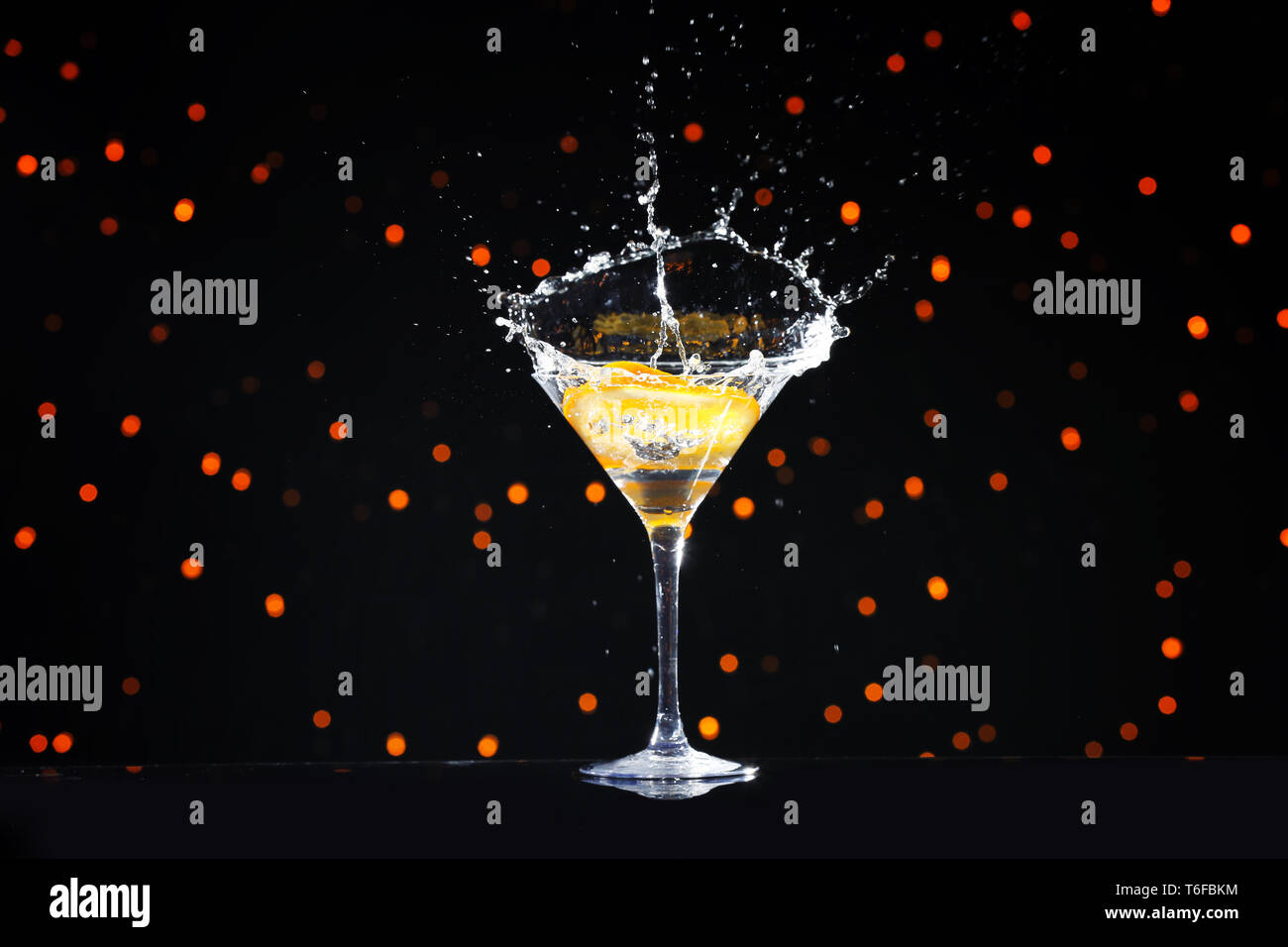 Verre à cocktail éclabousser et tranche d'orange contre Lumières floues Banque D'Images
