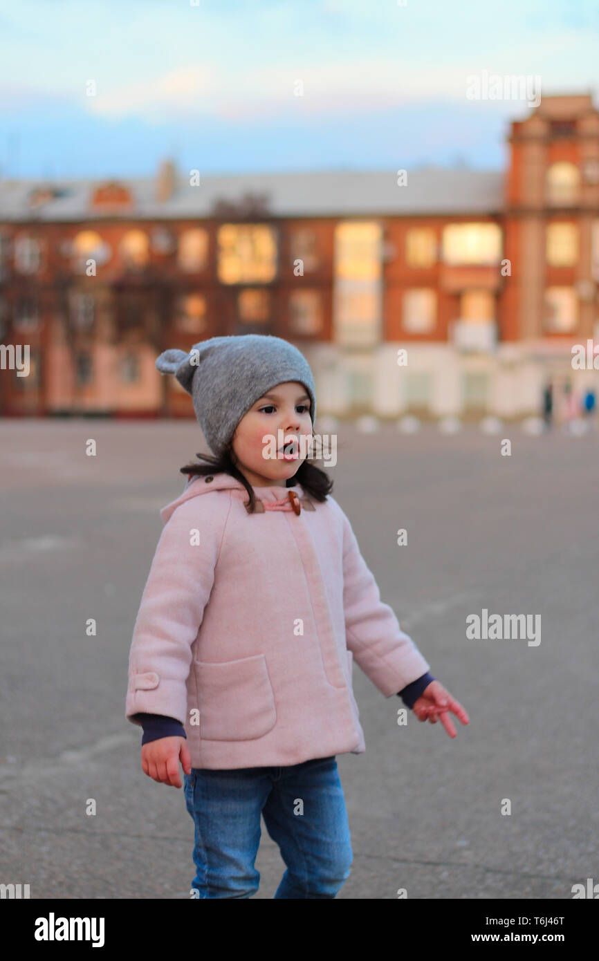 Peu surpris fille blanche marche dans la rue le soir. Portrait sur l'arrière-plan de la ville au coucher du soleil Banque D'Images