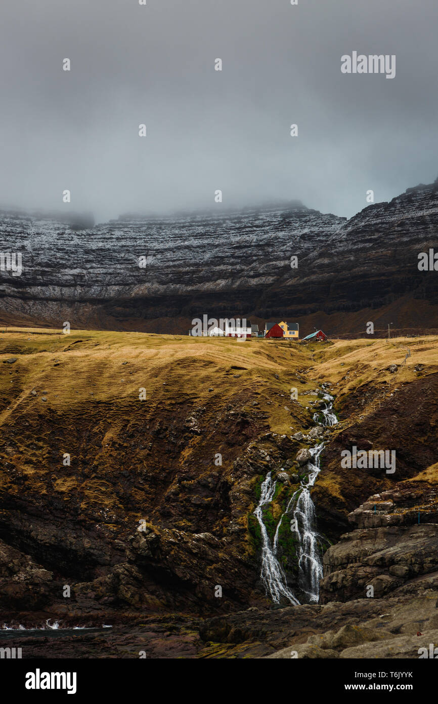 Petite cascade en face de maisons colorées en bois des îles Féroé typique dans le village Viðareiði en route vers Kap Enniberg (îles Féroé, Danemark, Europe) Banque D'Images