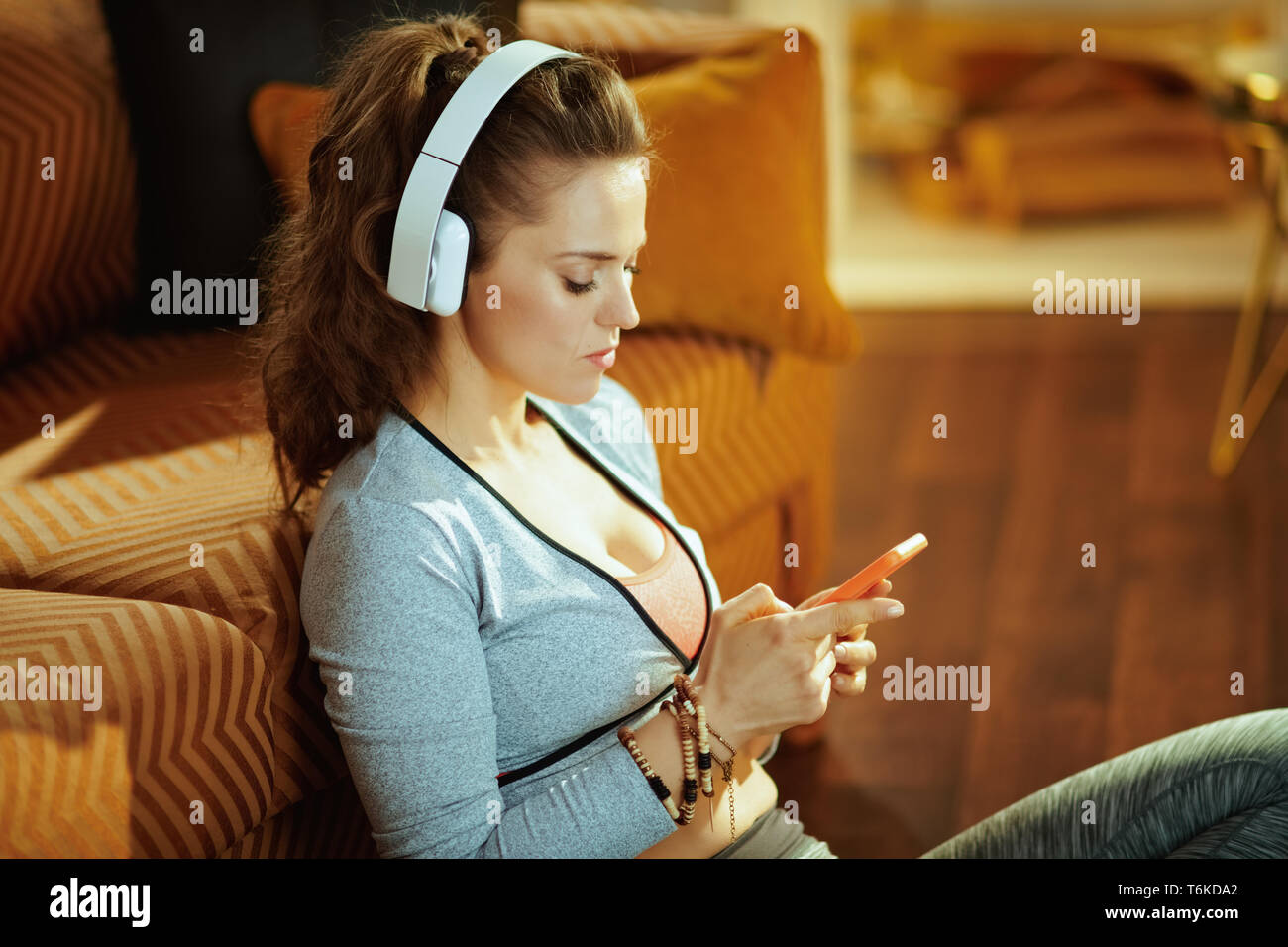 Femme en bonne santé en casque blanc en fitness vêtements dans le salon moderne l'envoi de message texte de téléphone. Banque D'Images
